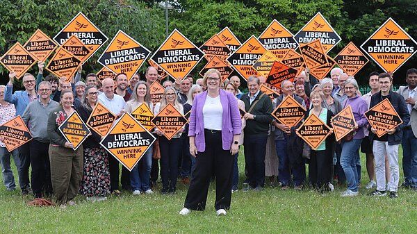 Zoe Franklin standing in front of a crowd of her supporters holding up golden Lib Dem diamonds.