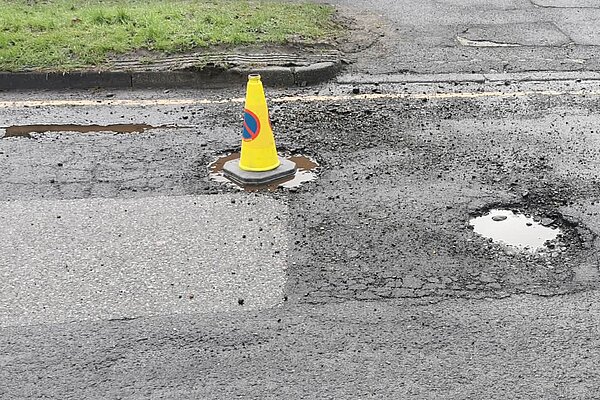 Traffic cone in one of many large potholes in road