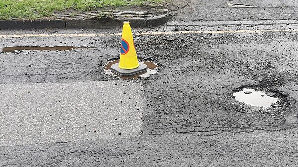 Traffic cone in one of many large potholes in road